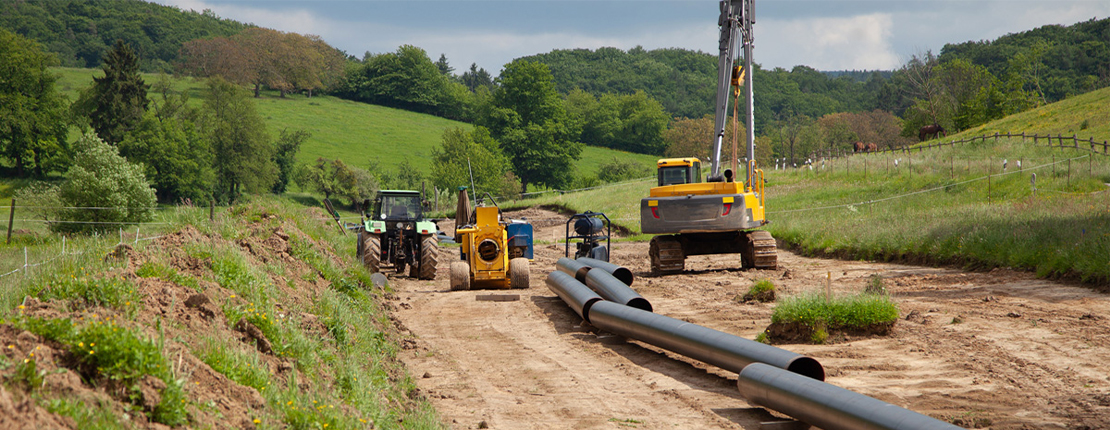 UnionStahl: Verlegung langlebiger Stahlrohre für Rohrkonstruktionen auf einer Baustelle mit Bagger und Traktor.