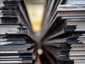 Grob- und Bandbleche nebeneinander auf Lager, zur Veranschaulichung der Unterschiede in Dicke, Form und Anwendung